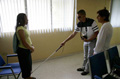 Señor invidente usando bastón. Enfrente persona joven mujer viendo sus avances.