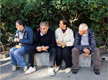 En la foto aparecen cuatro personas mayores sentadas en un banco de un parque observando lo que ocurre alrededor sin interactuar entre ellas.