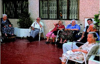 En la imagen aparecen un grupo de personas mayores sentadas en el exterior de un centro residencial y que no interactúan entre sí.