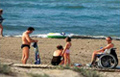 La imagen es de una playa en la que se encuentra n cuatro personas, una de ellas usuaria de silla de ruedas.