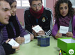 En la imagen aparecen un grupo de jóvenes sentados alrededor de una mesa haciendo una dinámica de grupo. Cada uno lleva un papel en la mano con un nombre.