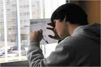 En la imagen aparece un chico joven cumplimenado un cuestionario. Está escribiendo apoyándose en el cristal de una ventana.