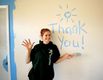 Chica con sudadera que ha pintado las palabras “Thank you” con pintura azul en una pared blanca.