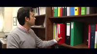 Se ve  a Alejandro uno de los protagonistas del caso práctico cogiendo un archivador de color rojo de una estantería en uno de los despachos de la empresa.