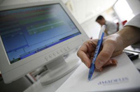 Aparece una imagen de la mano de una persona utilizando un bolígrafo, un papel y un ordenador trabajando en la oficina.