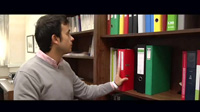 Se ve a uno de los protagonistas del caso práctico cogiendo un archivador de color rojo de una estantería en uno de los despachos de la empresa. 