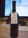 Botella de vino junto a un ordenador y un teclado en la mesa.