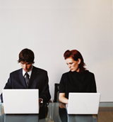  Imagen que muestra a dos empelados de una empresa trabajando con sus ordenadores portátiles, mientras uno de ellos se fija en lo que está escribiendo el otro.