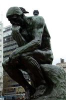 Estatua de un hombre pensativo con palomas encima.