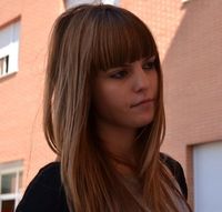 Primer plano de Sandra con expresión triste. Detrás de ella se ve un edificio de ladrillo.