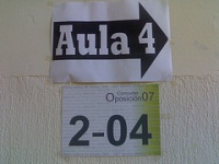 Oposición. Cartel con una flecha que indica la dirección a seguir para llegar al aula 4 donde se realiza el concuso oposición 07 según se indica en otro cartel inferior.