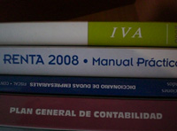En la imagen se ve un Plan General de contabilidad sobre el que se sitúan apilados encima otros libros entre ellos una guía de renta y uno de IVA.