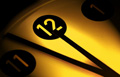 En la fotografía se ve un número doce que parece formar parte de un reloj, con una dos agujas que lo señalan, sobre un fondo amarillo difuminado. 