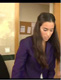 Imagen de una chica joven morena de pelo largo, en plano corto, que lleva una traje de chaqueta en azul marino y que se ve situada delante de la puerta de una oficina, su nombre es Luna.