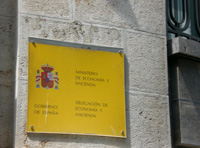 En la imagen se muestran una fachada de piedra en un plano muy corto, con una placa de fondo amarillo con el escudo de España y en la que se lee Ministerio de Economía y Hacienda, Delegación de Economía y Hacienda.