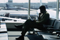 Persona sentada delante de una cristatelera en la sala de espera de un aeropuerto leyendo unos documentos.