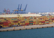 Vista aérea de contenedores en el muelle de un puerto con unas grúas pórtico detrás.