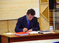Hombre con traje azul sentado corrigiendo exámenes.
