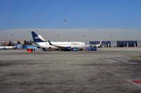 Avión en la pista de un aeropuerto con unos hangares al fondo.