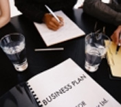 Plan de empresa. Mesa con vasos y un ejecutivo escribiendo.