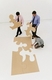 Tres personas, dos hombres vestidos con camisa y corbata, de pie, y una chica en el suelo intentan formar un puzzle, cada uno de los hombres llevan una pieza en la mano y la chica intenta unirlas. El fondo de la imagen es blanco y las piezas del puzzles son grandes y de color marrón.