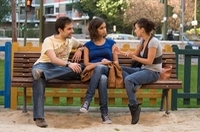 Ana García con sus compañeros. Aparecen tres chicos jóvenes en actitud informal sentados en un banco en la calle charlando.