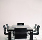 Mesa de ejecutivo, con solo unas carpetas en la mesa y seis sillas preparadas para una reunión. Las sillas y la mesa son de color negro y de acero, todo con fondo blanco.