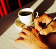 Dos manos, una escribiendo sobre la otra y una taza de café al lado.