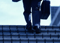 Vista de las piernas de un ejecutivo subiendo unas escaleras con un maletín en la mano.