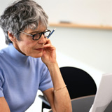 Mujer de cierta edad con una blusa de color azul y gafas, lee atentamente una documentación, su actitud es de concentración.