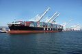 Vista inferior desde proa / babor de un buque portacontenedores atracado en el muelle de Oakland, california, Estados Unidos. Las grúas del muelle tienen las plumas alzadas.