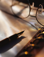 Pluma estilográfica y gafas sobre un documento en una carpeta de anillas.