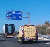 Transporte terrestre. Un camión de dimensiones especiales circulando por una autovía y una furgoneta detrás de color amarillo. Se puede ver un panel informativo de direcciones azul en la autovía.