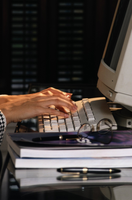 Imagen de una persona facturando. Aparecen las manos de una mujer tecleando un ordenador, junto al teclado dos libros apilados con unas gafas encima.
