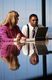 Dos personas observan un ordenador portátil mientras están sentadas delante de una mesa de reuniones. De fondo se observa unas cristaleras y unas cortinas.