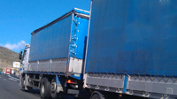 Deberes. Camión con remolque circulando por una autovía. Al fondo de la imagen se observan vehículos que circulan por dicha autovía. El tiempo está despejado.