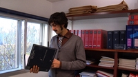 Hombre joven de mediana edad con bigote leyendo unos documentos.