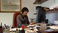 Hombre joven con bigote sentado delante de un ordenador.