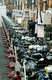 Fábrica de motos en la que se observa un operario manipulando un control numérico, y una fila enorme de motos por terminar de montar que se pierde en la perspectiva de la foto.
