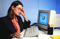 Archivo. Trabajadora sentada frente a un ordenador, con unas gafas puestas. El monitor está encendido y encima de la mesa se observa un teclado y un lapicero lleno de bolígrafos.
