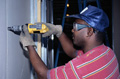 Operario trabajando con un taladro, realiza un orificio en una pared y lleva guantes, gafas de seguridad y una gorra..