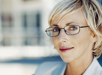 Mujer en primer plano con pelo rubio y corto y una gafas. Vestida de forma elegante.