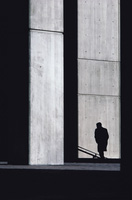 Un edificio de hormigón entre sombras, con la sombra de la figura de una persona de fondo.