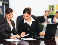 Fases del equipo 4. Dos mujeres elegantemente vestidas repasaon unos documentos con un portátil delante.