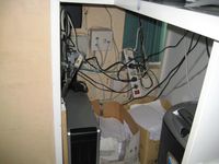 Enchufe sobrecargado. Un enchufe tiene una regleta de enchufes conectada, mal dispuesta, de la que salen un montón de cables hacia distintos aparatos.