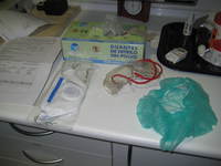 EPI. Sobre una mesa se ve una caja de guantes desechables, unas gafas protectoras, una mascarilla protectora, y un gorro desechable.