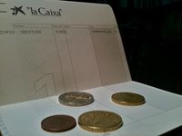 Fotografía en la que aparecen una cartilla o libreta de una cuenta corriente, y cuatro monedas de diversos tamaños. La cartilla aparece abierta y las cuatro monedas encima de una página.