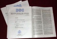 Fotografía sobre fondo negro de varios ejemplares del Boletín Oficial del Estado (B.O.E). Uno de los ejemplares está abierto y se puede ver el texto del boletín escrito a dos columnas.