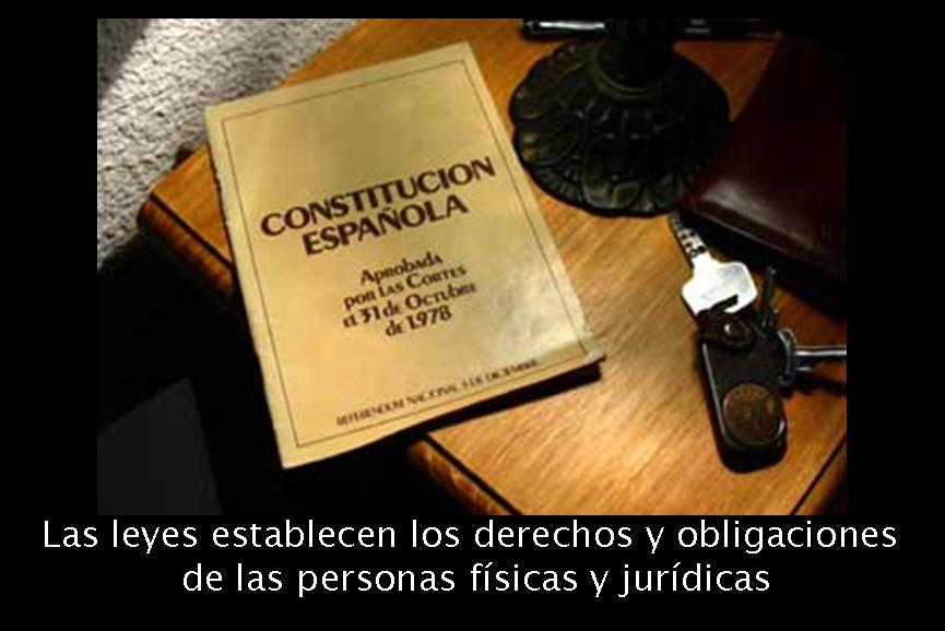 Fotografía en la que se ve la constitución española encima de una mesita. El libro de la constitución es un libro con portada blanca y letras negras, y esta puesto en la mesa de forma que una esquina queda al aire. Aparte de la constitución, en la mesa se ven unas llaves, el pie de lo que podría ser una lámpara y la esquina de lo que podría ser una cartera. Debajo de la fotografía se puede leer un texto que pone “Las leyes establecen los derechos y obligaciones de las personas físicas y jurídicas”.