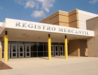 Fotografía en la que se puede ver la puerta de entrada del registro mercantil. La puerta de entrada es una puerta muy amplia y encima de ella hay un cartel que pone Registro Mercantil. El edificio no es muy alto, por la parte de la puerta de entrada tiene una planta de altura y a su derecha, hay un edificio adjunto de dos o tres plantas.